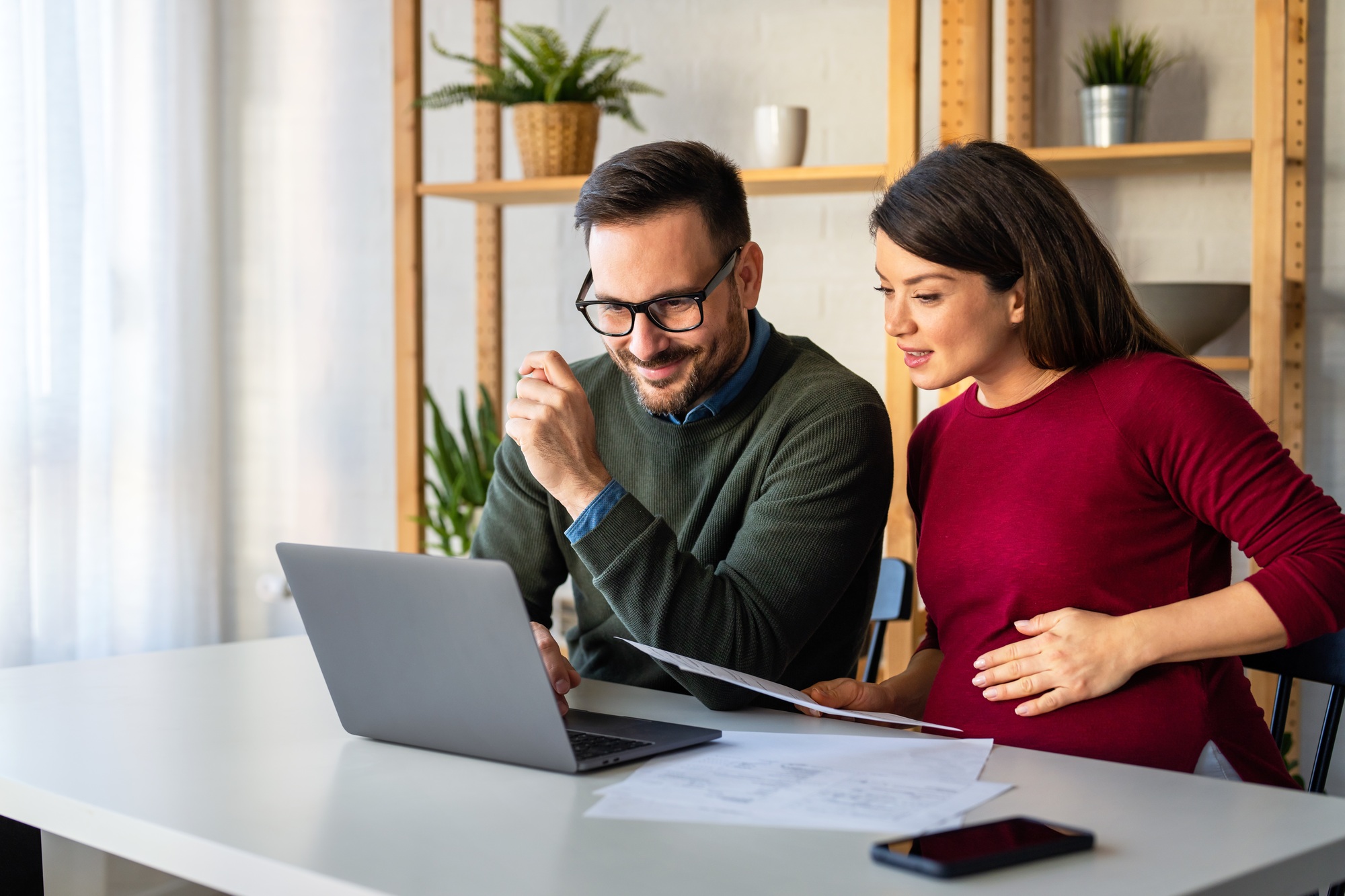 Pregnant wife with husband making online payment using credit card on laptop at home